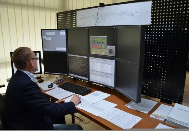 Dyżurny ruchu PKP analizuje dane na wielu monitorach. Na biurku dokumenty i klawiatura.