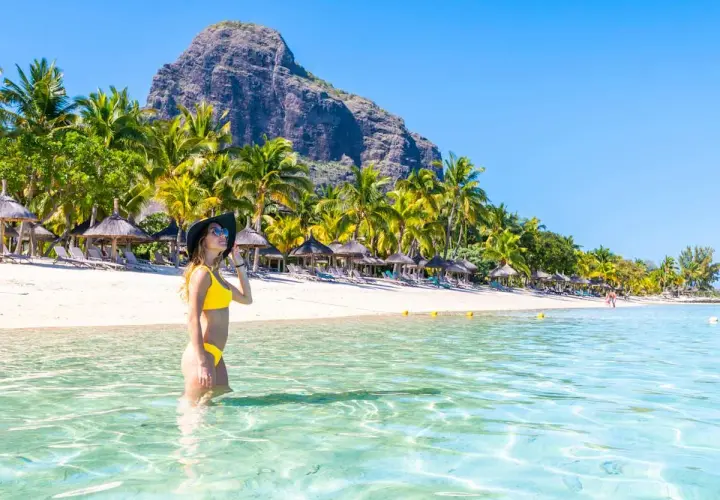 Frau im Bikini genießt das kristallklare Wasser an einem Traumstrand von Mauritius. Palmen und ein Berg im Hintergrund.