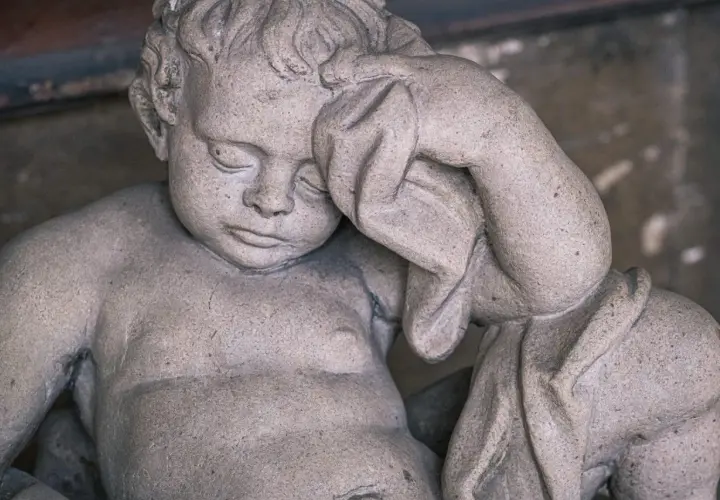 Kamienna rzeźba dziecka z zasłoniętymi oczami, jakby śniło o śmierci rodziców.