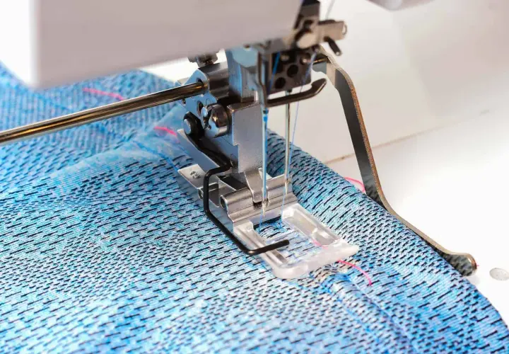 Sewing machine creating a coverstitch hem on blue patterned fabric.