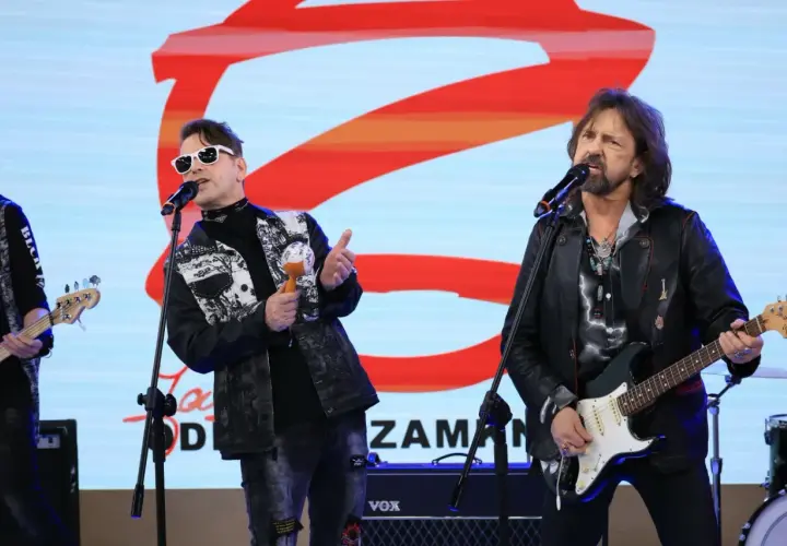 Zespół rockowy na scenie, wokalista w białych okularach i kolorowej kurtce, grający na marakasach. Obok gitarzysta w skórzanej kurtce. W tle logo "Jary Oddział Zamknięty".