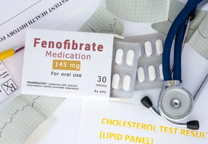 Opakowanie leku Fenofibrate 145 mg, tabletki, obok stetoskopu i wyników badań cholesterolu. Lipanthyl pomaga w leczeniu.