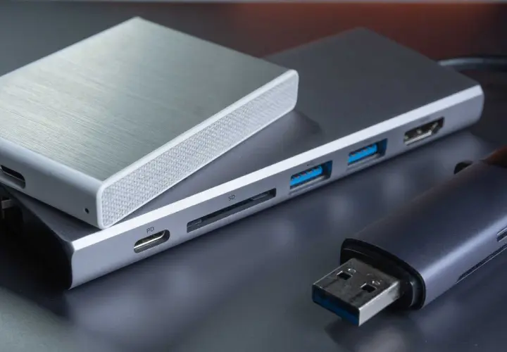 Ein silbernes Gehäuse für eine externe Festplatte liegt auf einem USB-Hub mit SD-Kartenleser und mehreren USB-Anschlüssen. Daneben ein USB-Stick.