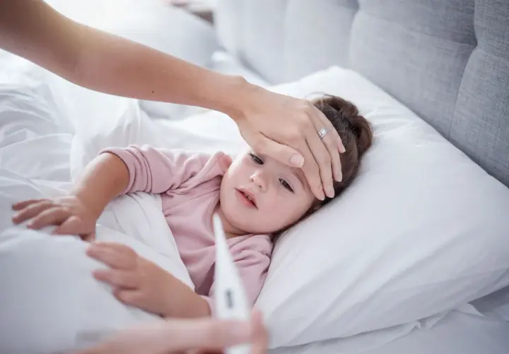 Madre revisa la fiebre de su hija. Si la fiebre persiste, considera el ibuprofeno para bebes.