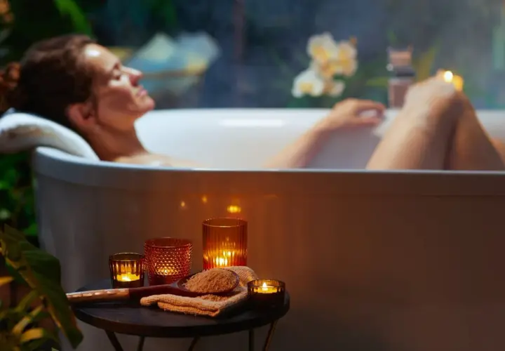 Kobieta relaksuje się w wannie, otoczona świecami i roślinnością. Czas na spokojne zabawy w wannie.