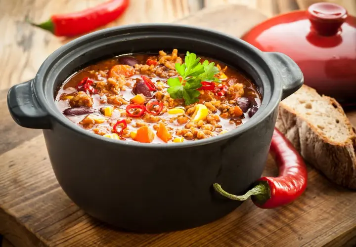 Un plat de chili mijoté dans une cocotte en fonte, parfait pour savoir si l'on peut mettre une cocotte en fonte au four. Accompagné de pain et de piments.