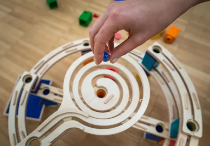 Mano che rilascia una biglia blu su una pista a spirale in legno, parte di giochi con le biglie.