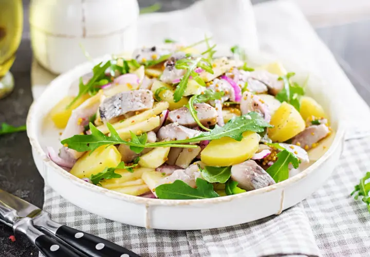 Salade de pommes de terre et hareng à l'huile, garnie de roquette et d'oignons rouges. Une recette simple et savoureuse.