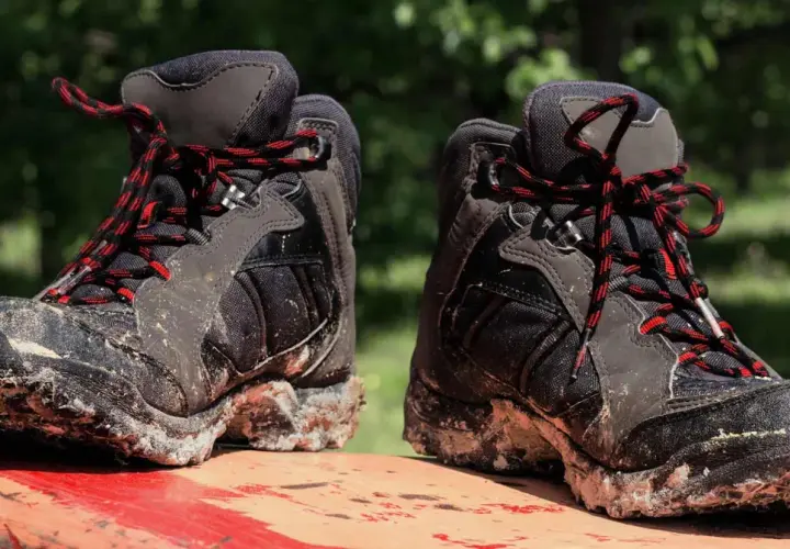 Mud-caked hiking boots with red and black laces sit on a red surface. These boots show signs of heavy use, hinting at how long do hiking boots last.