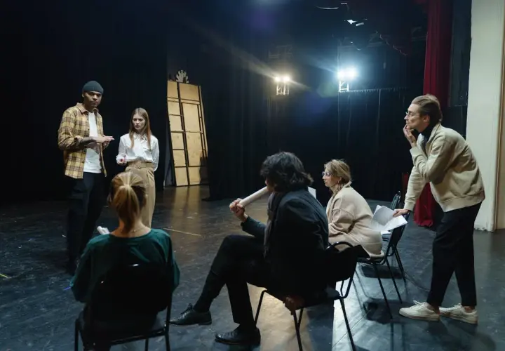 Grupa ludzi na scenie, dyskutująca o sztuce. Zastanawiają się, ile zarabia reżyser w Polsce, analizując scenariusz.