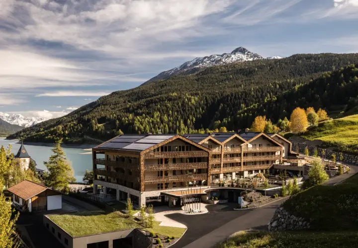Das Gerstl Family Retreat, un hotel moderno con pannelli solari, si affaccia su un lago alpino e montagne boscose.