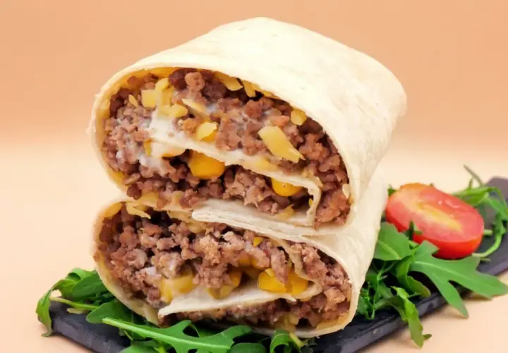 Pyszna tortilla z mięsem mielonym, kukurydzą i serem, przekrojona na pół, z rukolą i pomidorkiem.