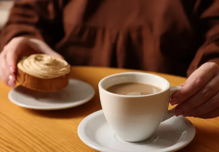 Kawa przed snem z ciastkiem. Dłonie trzymają filiżankę kawy i słodki deser na drewnianym stole.