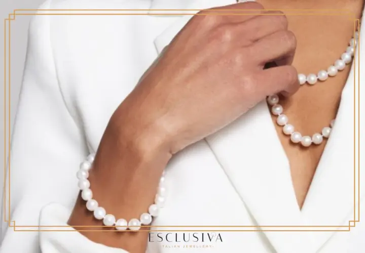 Dłoń w białej marynarce dotyka naszyjnika i bransoletki z pereł. Ich subtelne piękno podkreśla elegancję, ukazując niezwykłe perły właściwości.
