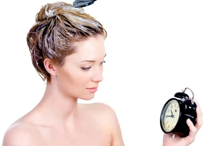 Mujer con tinte en el pelo, mirando un reloj. El tiempo es crucial para un tinte pelo perfecto.