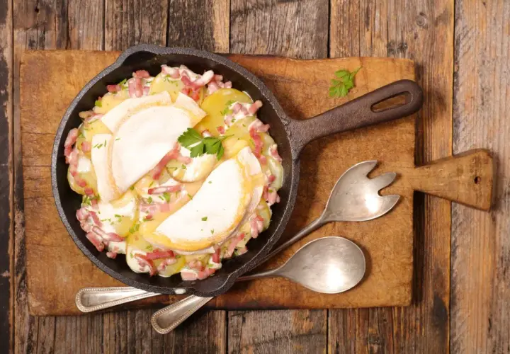 Plat de pommes de terre gratinées avec lardons et fromage fondant, servi dans une poêle en fonte. Un plat avec charcuterie réconfortant.
