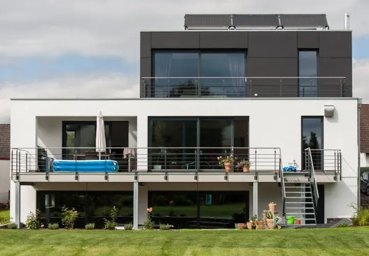 Moderne Hausumbau-Ideen: Vorher-Nachher-Vergleich eines weißen Hauses mit dunklem Anbau, Balkon und Pool.