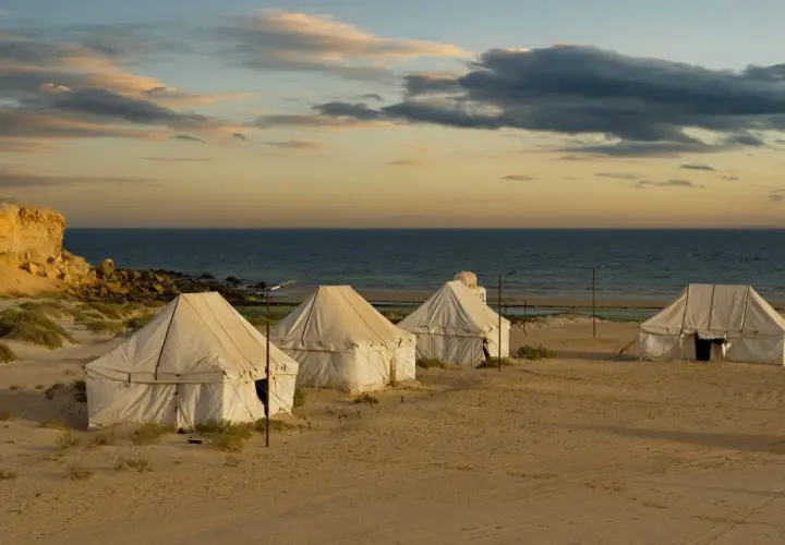Namioty na piaszczystej plaży nad oceanem o zachodzie słońca.