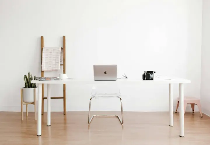 Ein moderner Arbeitsplatz mit einem weißen Schreibtisch, Laptop, Kamera und einer Pflanze. Perfekt für alle, die einen **tisch selber bauen** möchten.