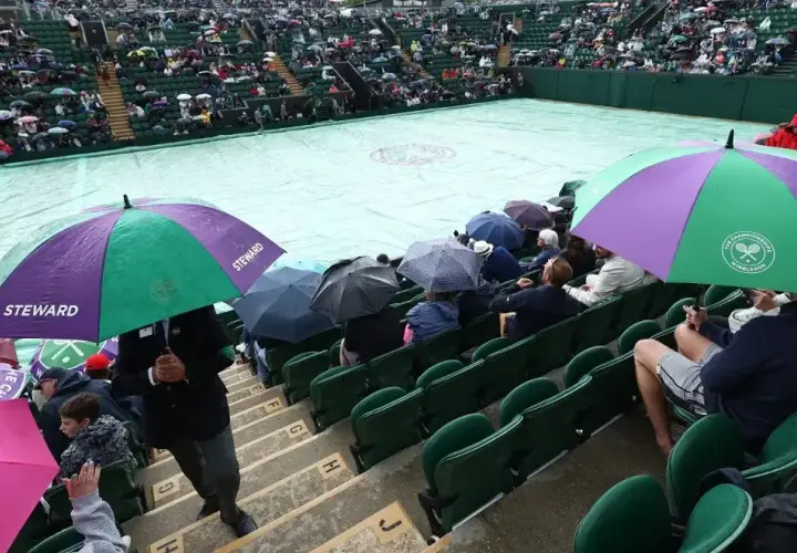Wimbledon deszcz przerwał mecz. Widzowie siedzą pod parasolami, a kort przykryty jest plandeką.