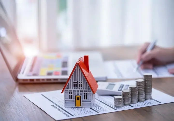 Model domu, stos monet i kalkulator na dokumencie "House Insurance". To symbol ubezpieczenia pomostowego, które chroni Twój dom.