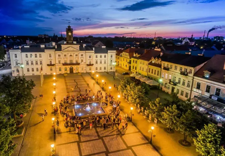 Wieczorny stary rynek płock, z ratuszem i fontanną, oświetlony latarniami, z tłumem ludzi.