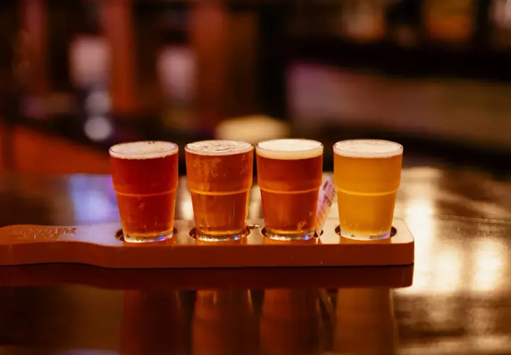 Quatre verres de bière, de différentes couleurs, sur un plateau en bois. Une dégustation de bière, pas de bière chaude ici !