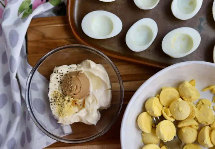 Ingredients for miso egg salad: mayonnaise, miso paste, pepper, and separated egg yolks in a bowl. Halved hard-boiled eggs are on a tray.