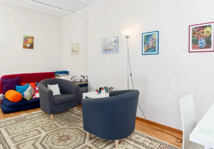 Accogliente studio psicologo in casa, con divano letto, poltrone, tappeto e quadri colorati.