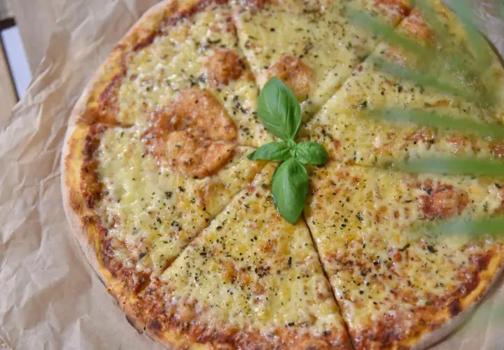 Pyszna pizza z roztopionym serem, posypana ziołami i udekorowana listkiem bazylii. Idealny ser do pizzy dla każdego smakosza.