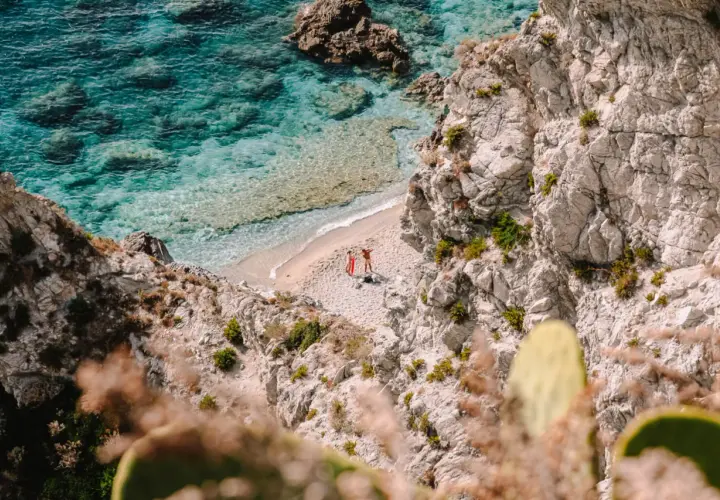 Malownicze kalabryjskie plaże z turkusową wodą i skalistymi klifami. Dwie osoby odpoczywają na piaszczystej plaży, ciesząc się słońcem.