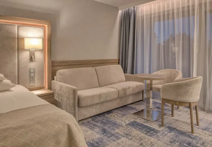 Przytulny pokój w hotelu 5 gwiazdkowym nad morzem: wygodna sofa, stolik z krzesłami i łóżko.