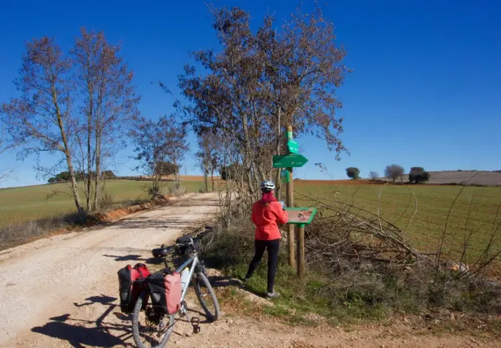 Ciclista consulta señalización en la **vía verde del Tajuña**. Bicicleta con alforjas lista para la aventura.