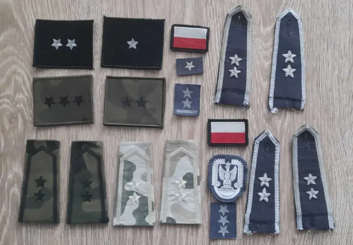Różne stopnie wojskowe na pagonach i naszywkach, w tym polska flaga.
