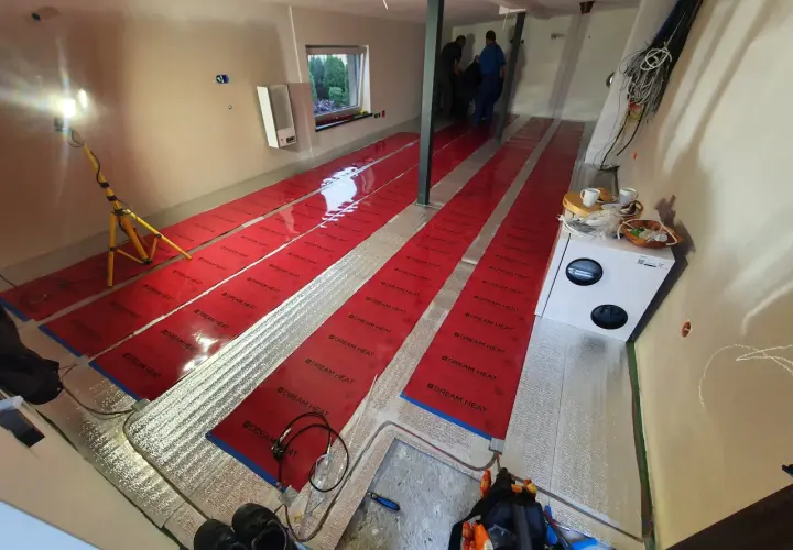 Instalacja folii grzewczej "Dream Heat" na podłodze. Czy folia grzewcza jest oszczędna? Montażyści pracują, przygotowując pomieszczenie do ogrzewania.