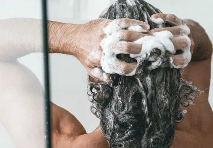 Persona disfrutando de un relajante lavado de cabeza con abundante espuma de champú.