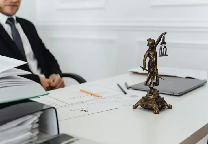 Une statue de la justice, symbole du juge de l'exécution, trône sur un bureau avec des documents et un homme en costume.