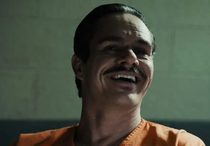Lalo Salamanca ler skrattande i en orange fängelsedräkt, hans mustasch framträder tydligt.