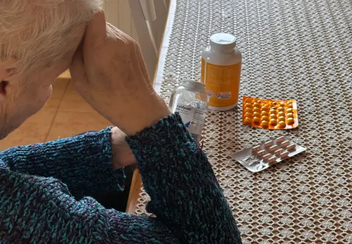 Osoba w swetrze z lekami na stole. Zastanawia się, renta wdowia komu przysługuje, szukając odpowiedzi.