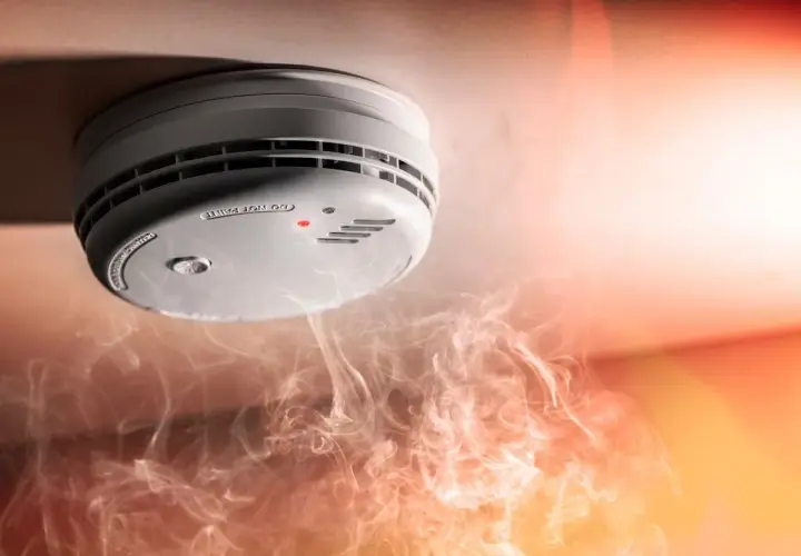 Detector de humo en el techo, rodeado de humo. Ilustra cómo funciona un detector de humo al alertar sobre el peligro.