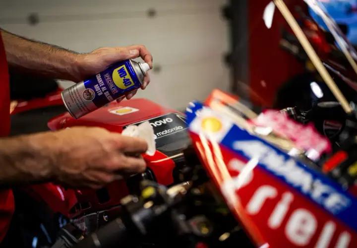 Mani che spruzzano WD-40 su una moto rossa per la lucidatura plastica, in preparazione per la gara.