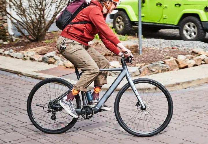 Enjoying the benefits of electric bikes: a person rides a sleek e-bike past a green Jeep, showcasing an eco-friendly commute.
