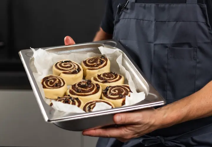 Manos sostienen una bandeja con deliciosos rollitos de canela listos para hornear.