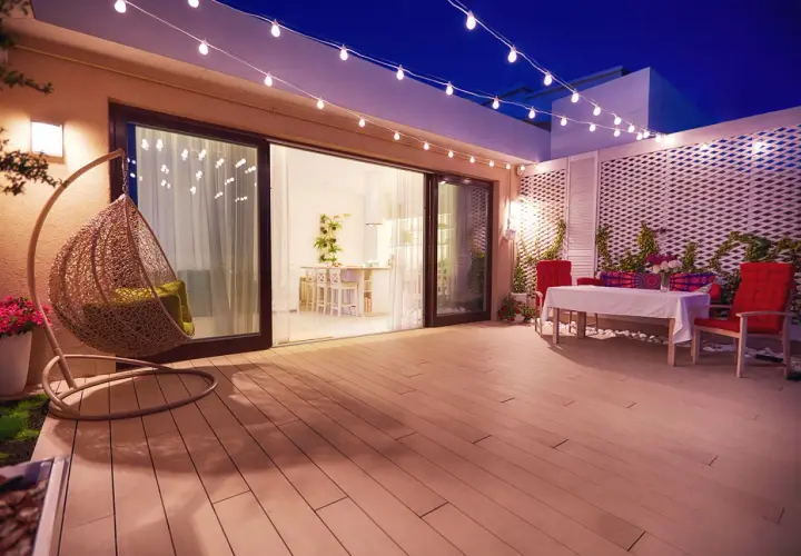 Terraza con silla colgante y mesa, iluminada por una guirnalda de luces. La pantalla lámpara plisada ilumina el ambiente.