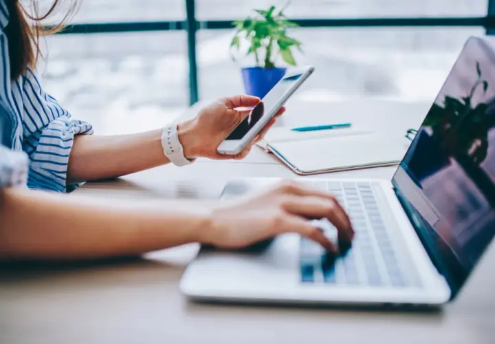 Kobieta korzysta z telefonu i laptopa, szukając informacji, jak podłączyć internet z telefonu do komputera.