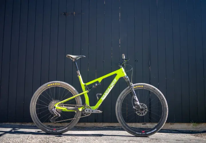 A bright green Santa Cruz Blur mountain bike is ready for a trail review, leaning against a dark wooden wall.