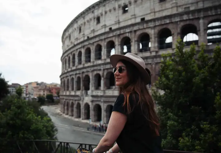 Une femme avec un chapeau et des lunettes de soleil admire le Colisée. Je visite Rome et ce moment est inoubliable.