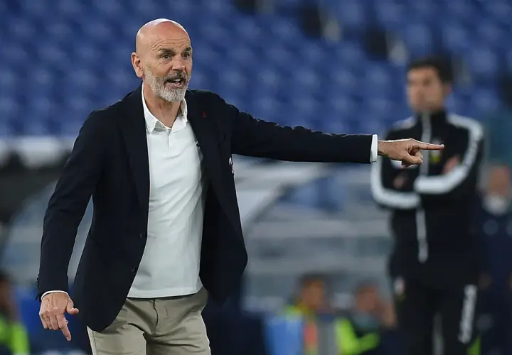 Trener Stefano Pioli w garniturze i białej koszulce polo wskazuje palcem, udzielając wskazówek na boisku.