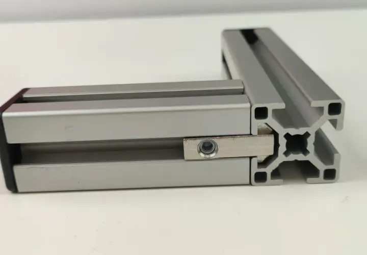 Dwa połączone profile aluminiowe konstrukcyjne tworzą kąt prosty. Widać element łączący z nakrętką.