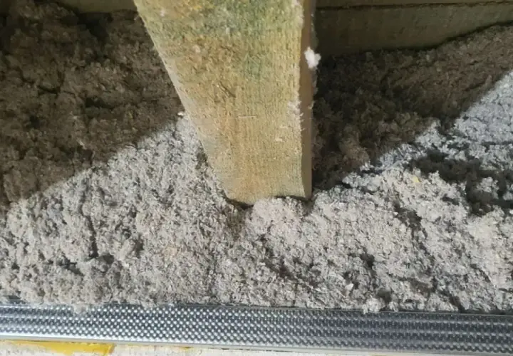 Luźna celuloza w szczelinach, drewniana belka i metalowa siatka. Wady ocieplenia celulozą widoczne przez nierównomierne rozłożenie materiału.